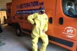 911 restoration mold removal tech standing next to work van wearing hazmat suit