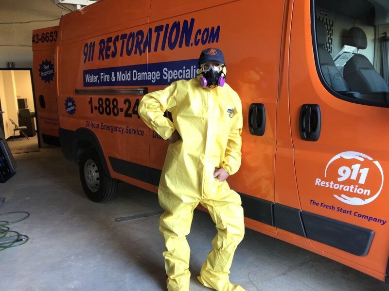 911 restoration mold removal tech standing next to work van wearing hazmat suit